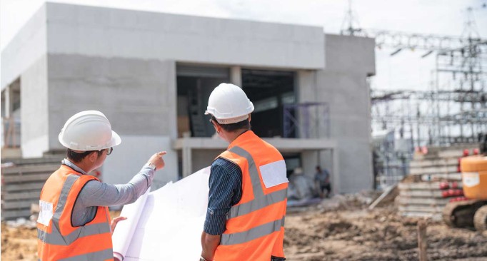 Due tecnici con casco e gilet controllano il progetto in cantiere